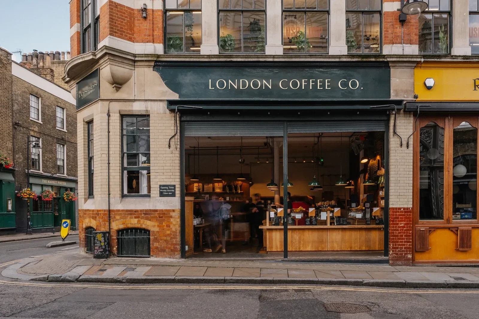 The London Coffee Co. shopfront on a Borough street corner, doors open onto a warm wooden counter